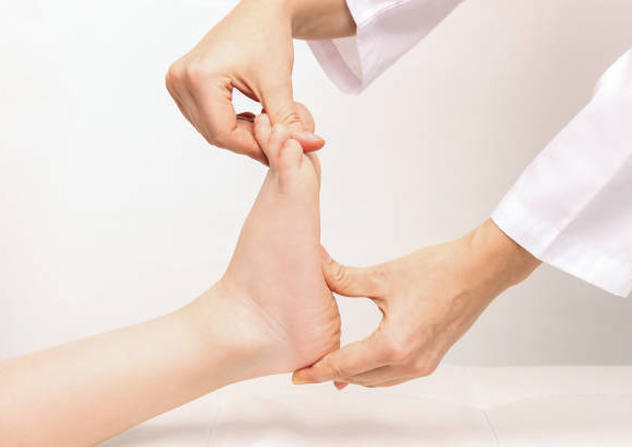 Examination of a child by an orthopedist. Cropped shot of female doctor holding a kid's foot in her hands.Pathology of bone structures, flat feet, injury. Foot treatment. Pain from uncomfortable shoes